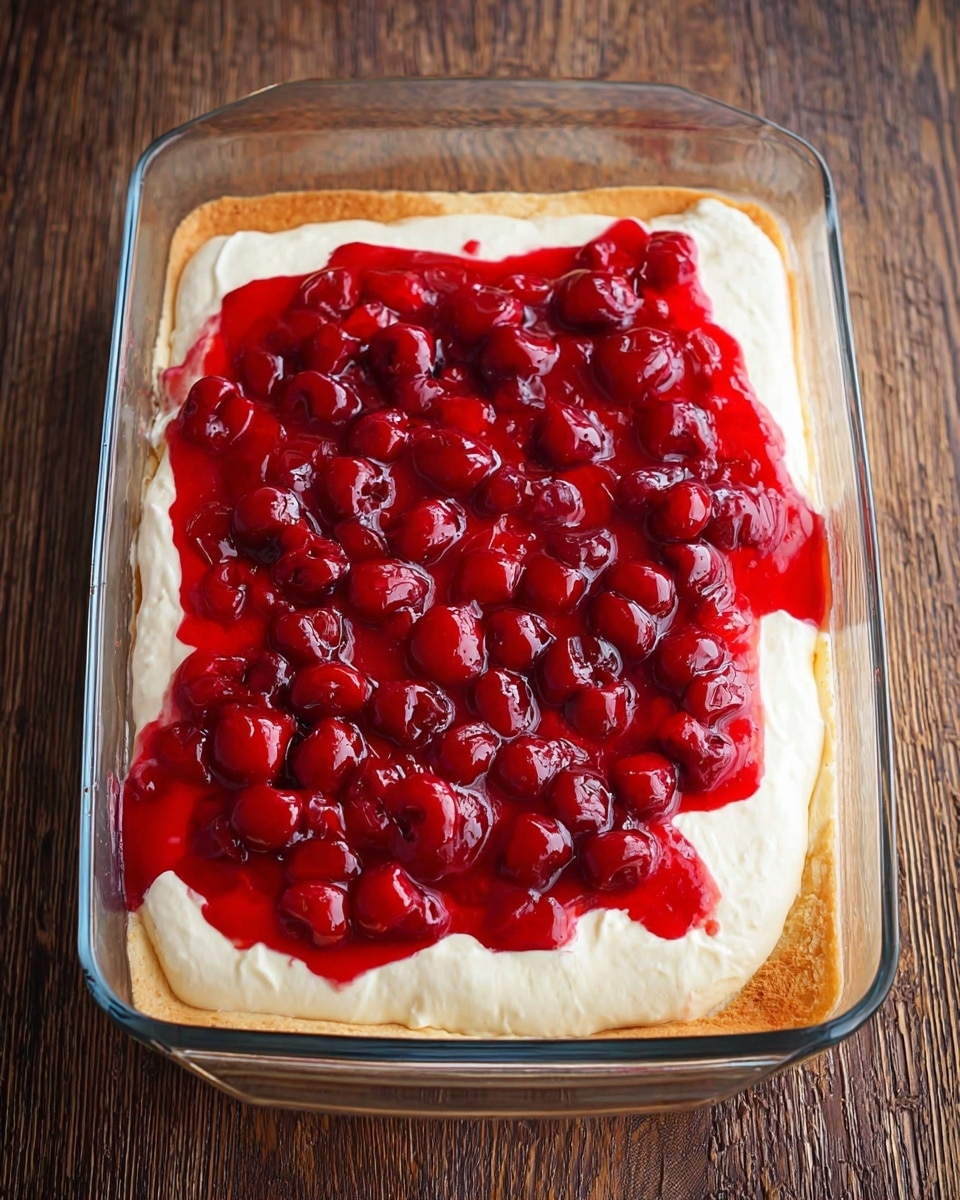 The image shows a glass rectangular dish filled with three visible layers of a dessert. The bottom layer is a soft light brown pastry or crust that fills the whole dish, with slightly folded edges. The middle layer is thick, smooth, and creamy white, spread evenly over the crust. The top layer is bright red cherry topping with whole cherries and shiny syrup, spread unevenly but covering most of the creamy layer. The dish rests on a wooden textured surface. photo taken with an iphone --ar 4:5 --v 7