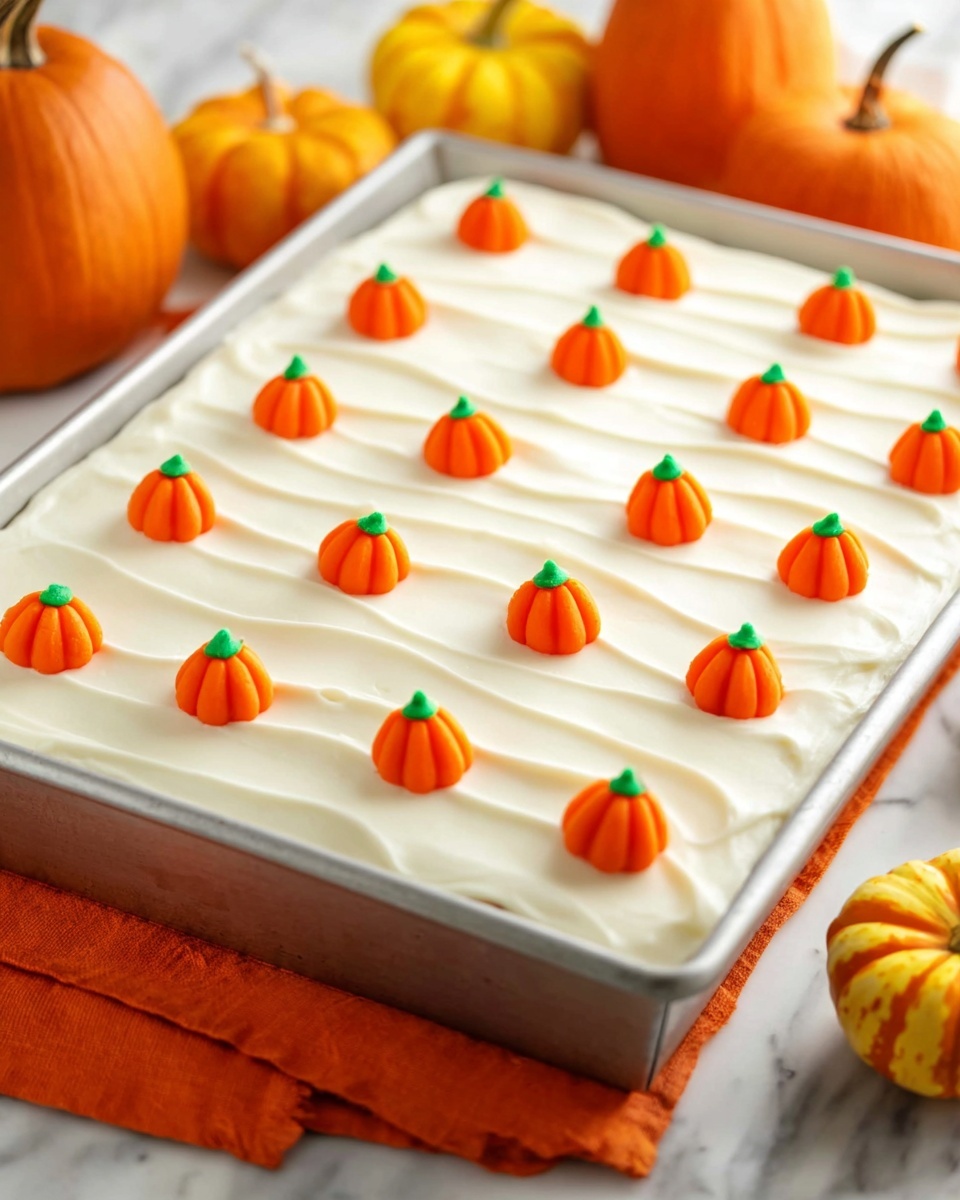 A large rectangular cake in a metal pan is covered with smooth, white frosting that has gentle wavy lines on its surface. The cake is decorated with small, bright orange pumpkin-shaped candies evenly spaced in rows across the top, each pumpkin featuring a small green stem. The pan rests on an orange cloth on a white marbled surface, with round orange and yellow pumpkins blurred in the background. The cake is pre-cut into squares beneath the candies. Photo taken with an iphone --ar 4:5 --v 7