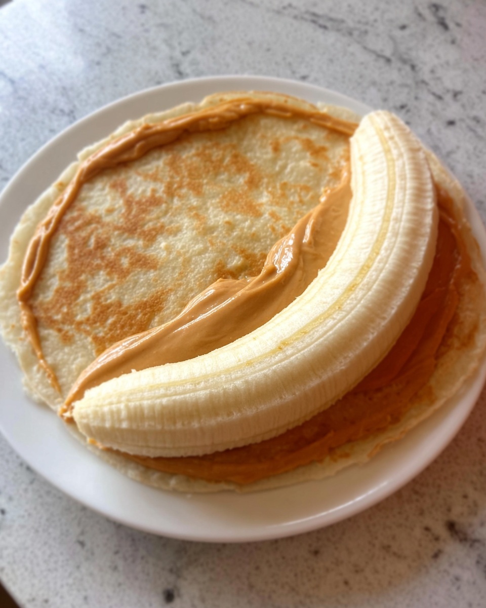 A white plate holds two thick pancakes stacked on top of each other, both with a light golden brown color and soft, smooth texture. On the right side of the top pancake, there is a long, curved white strip that appears creamy and smooth, lying over the pancakes. The plate is placed on a white marbled surface. Photo taken with an iphone --ar 4:5 --v 7