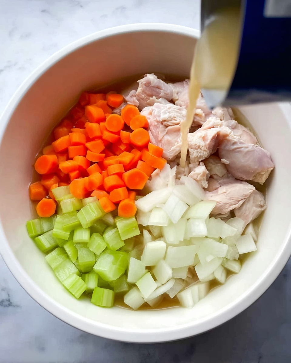 In a white bowl, there are three chopped vegetables placed in separate groups: bright orange small carrot pieces on the top left, light green celery slices on the bottom right, and white onion chunks on the bottom left. Below the vegetables, there is a layer of whole raw chicken pieces, partly covered by the vegetables. A light broth or liquid is being poured from a blue and white carton into the bowl, landing over the chicken and vegetables. The background underneath the bowl is a white marbled texture. photo taken with an iphone --ar 4:5 --v 7