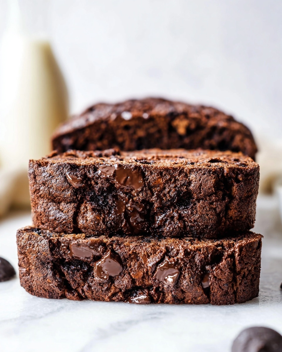 The image shows two thick slices of chocolate bread stacked close together on a white marbled surface. The bread has a dark brown color with a dense texture and is filled with melted chocolate chunks that shine on top and inside the slices. The layers of the bread include a moist chocolate base mixed with dark chocolate pieces, giving it a rich and soft look. The background is soft white, with a blurred light cream bottle shape in the back left side, focusing the attention on the detailed chocolate bread in the front. photo taken with an iphone --ar 4:5 --v 7
