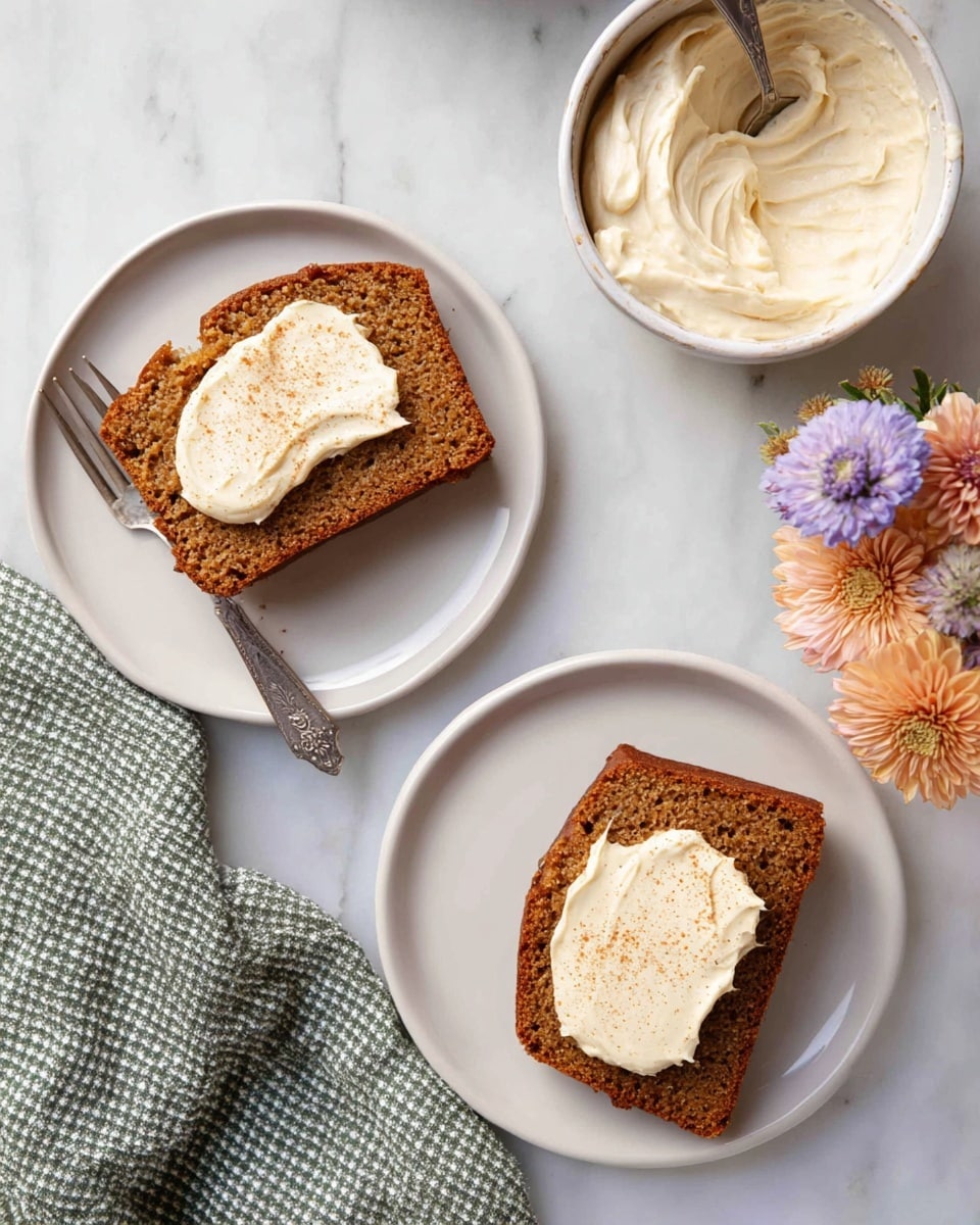 Two slices of brown spiced cake with a soft texture are placed on two white plates, each topped with a swirled layer of light cream cheese frosting sprinkled with a light dusting of cinnamon. The plates rest on a white marbled surface next to a white bowl filled with more creamy frosting and a spoon inside, with a small bouquet of soft purple and peach flowers nearby. A silver fork and a green and white checkered cloth are beside the bottom plate. Photo taken with an iphone --ar 4:5 --v 7