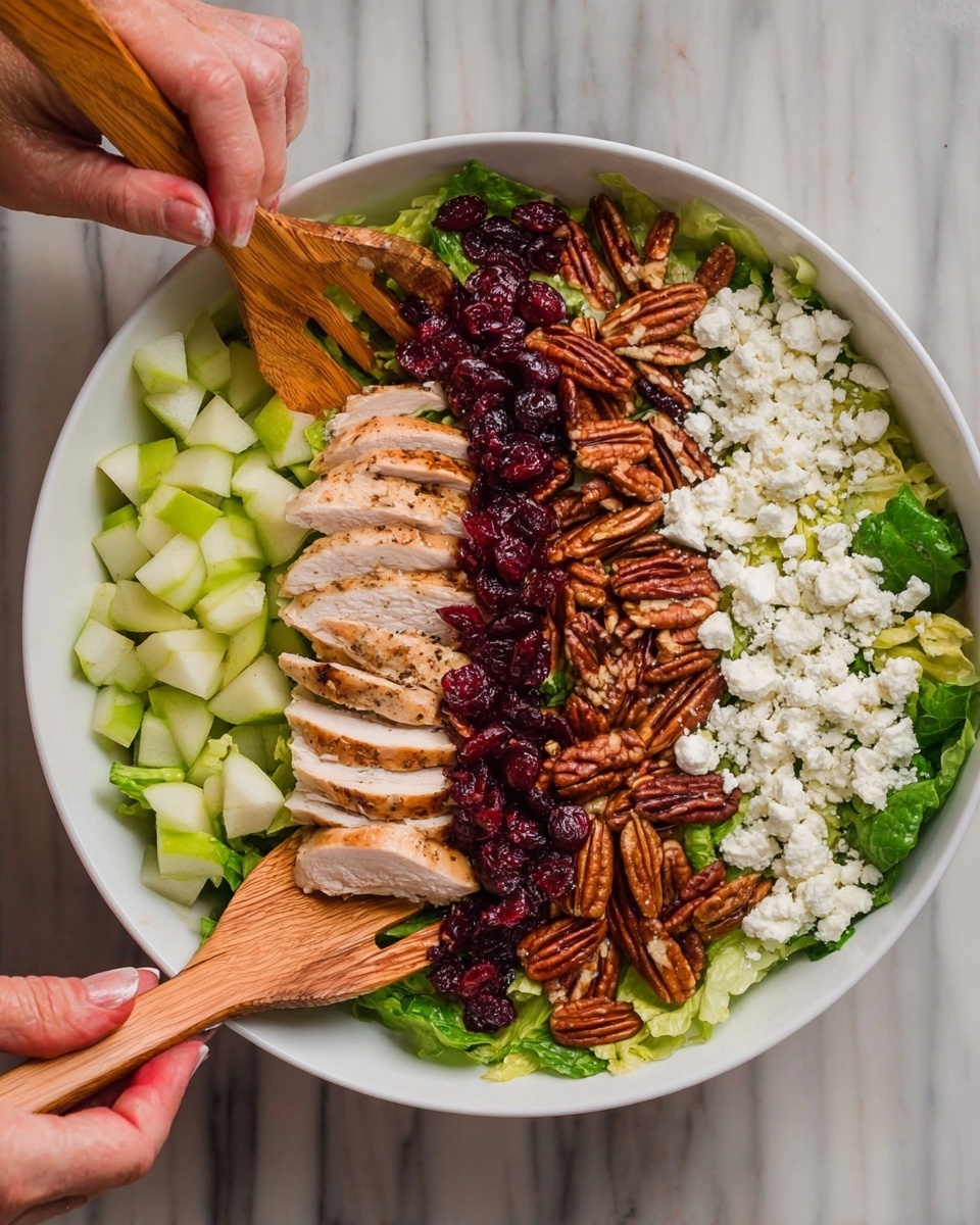 A white bowl contains a layered salad with green lettuce leaves at the bottom. Starting from the left, the first layer is small diced green pear pieces. Next to it is a thick line of sliced grilled chicken with a light brown, slightly crispy surface. In the middle, there is a strip of dried dark red cranberries. To the right of the cranberries, a layer of white crumbly cheese is placed. The last layer on the far right holds whole pecans with a glossy, rich brown color. Two wooden salad spoons are held by two woman's hands, one on each side, stirring the salad gently over a white marbled surface background. Photo taken with an iphone --ar 4:5 --v 7
