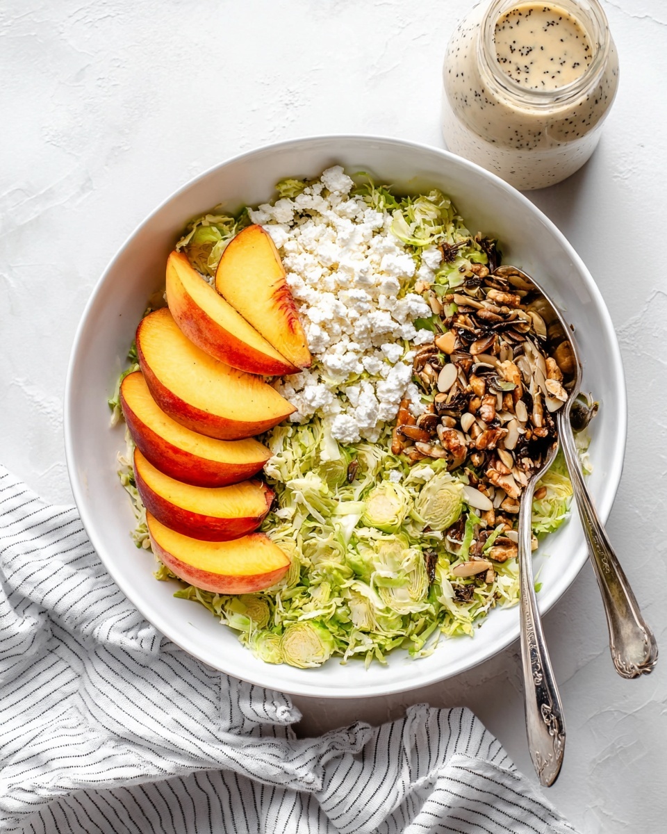A white bowl filled with a layered salad resting on a white marbled surface. The bottom layer is made of shredded light green Brussels sprouts spread evenly across the bowl. On the left side, there is a pile of white crumbled cheese with a soft and crumbly texture. To the right of the cheese, a heap of toasted mixed seeds and sliced nuts, showing brown and green colors with a crunchy texture. On top of the Brussels sprouts, arranged in a semicircle, are slices of fresh peach with yellow flesh and a smooth reddish-orange skin. Two silver spoons rest in the bowl, one on the left side and one on the right side. In the background, a striped white and gray cloth is draped next to a small, clear glass bottle filled with a creamy dressing with black specks. photo taken with an iphone --ar 4:5 --v 7