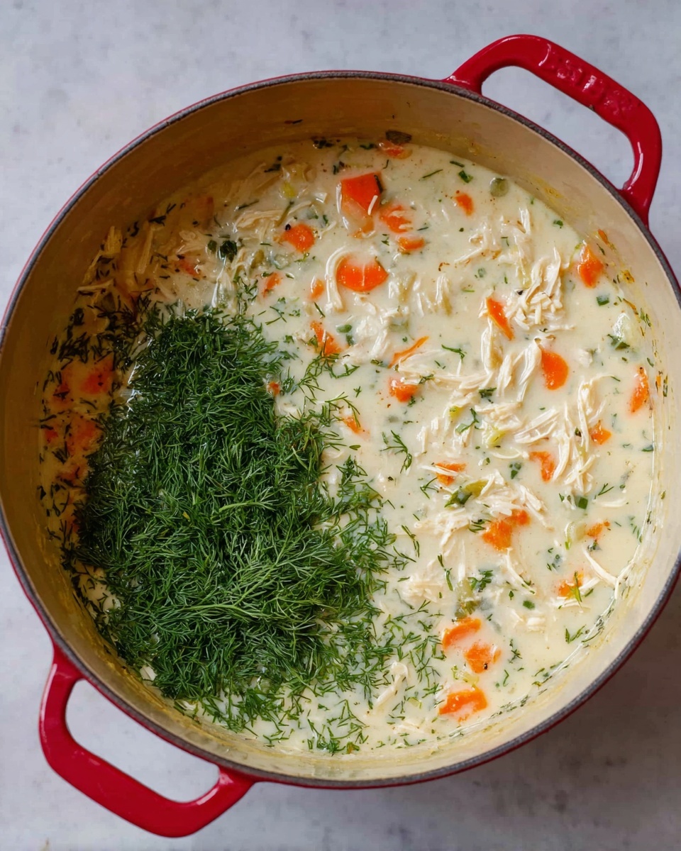 A top view of a red pot filled with creamy soup that has several layers visible; the base is a pale cream color with small pieces of orange carrots and white shredded chicken mixed in evenly. On one side of the soup, there is a large layer of fresh, finely chopped bright green dill herbs, creating a clear contrast with the creamy soup on the other side. The pot is placed on a white marbled surface. photo taken with an iphone --ar 4:5 --v 7