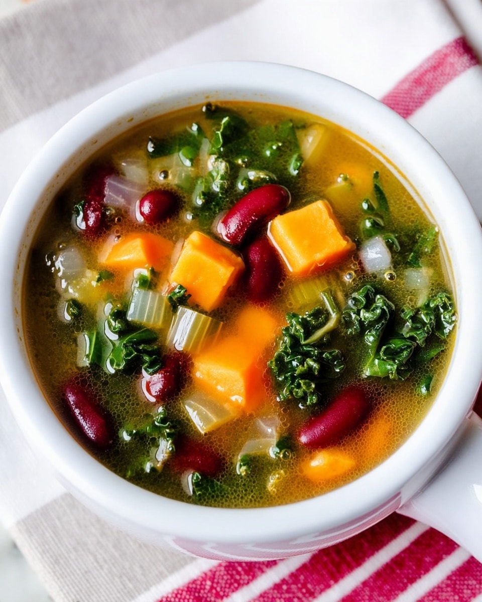 A white cup filled with a clear vegetable soup showing three main layers: bright orange cubes of squash or carrot, dark green curly kale leaves, and red kidney beans mixed with small pieces of translucent onion. The soup has a light broth with tiny bubbles on the surface. The cup is sitting on a white marbled surface with a white and red striped cloth underneath. photo taken with an iphone --ar 4:5 --v 7