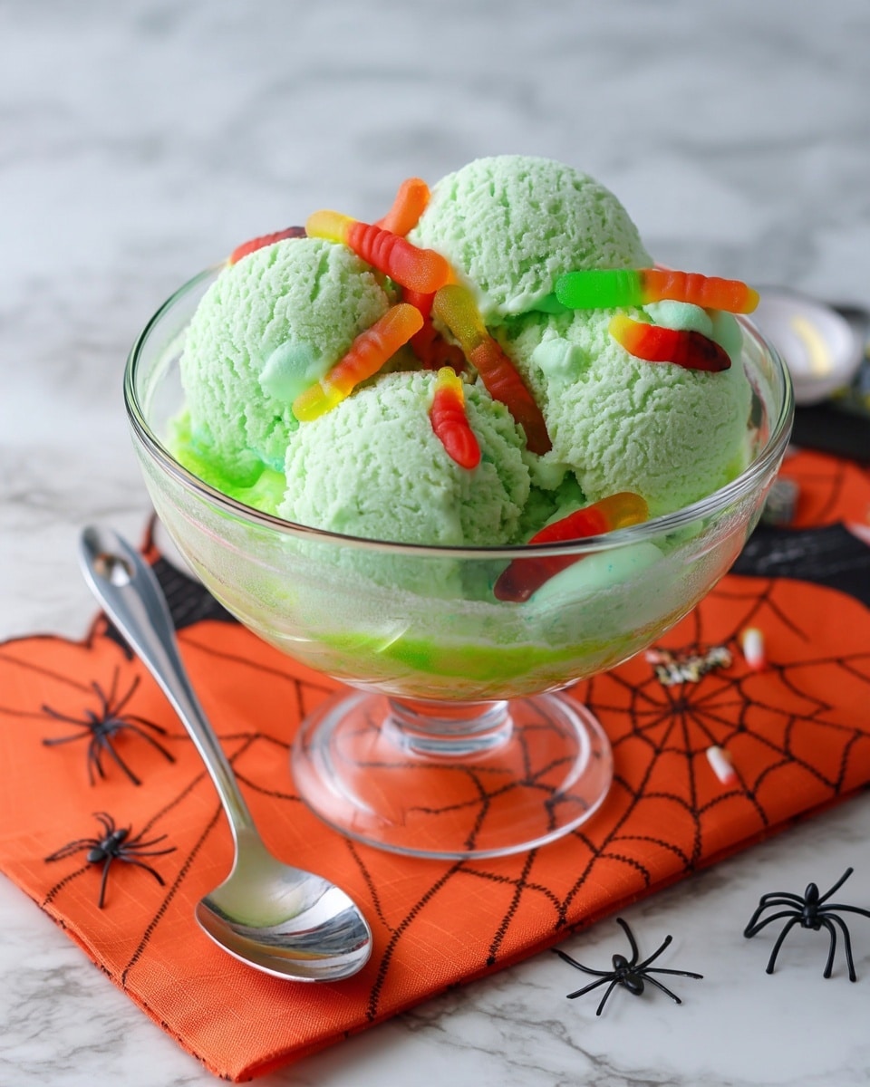 The image shows a clear glass bowl filled with a fizzy, bright green liquid as the base layer, topped with several scoops of light green ice cream that have a smooth and creamy texture. Scattered on the ice cream and surface are red and orange gummy worms, and there are also a few black plastic spiders placed around for decoration. A silver spoon rests inside the bowl on the right side. The bowl is sitting on a white marbled surface with orange napkins that have black spider web designs underneath. Photo taken with an iphone --ar 4:5 --v 7