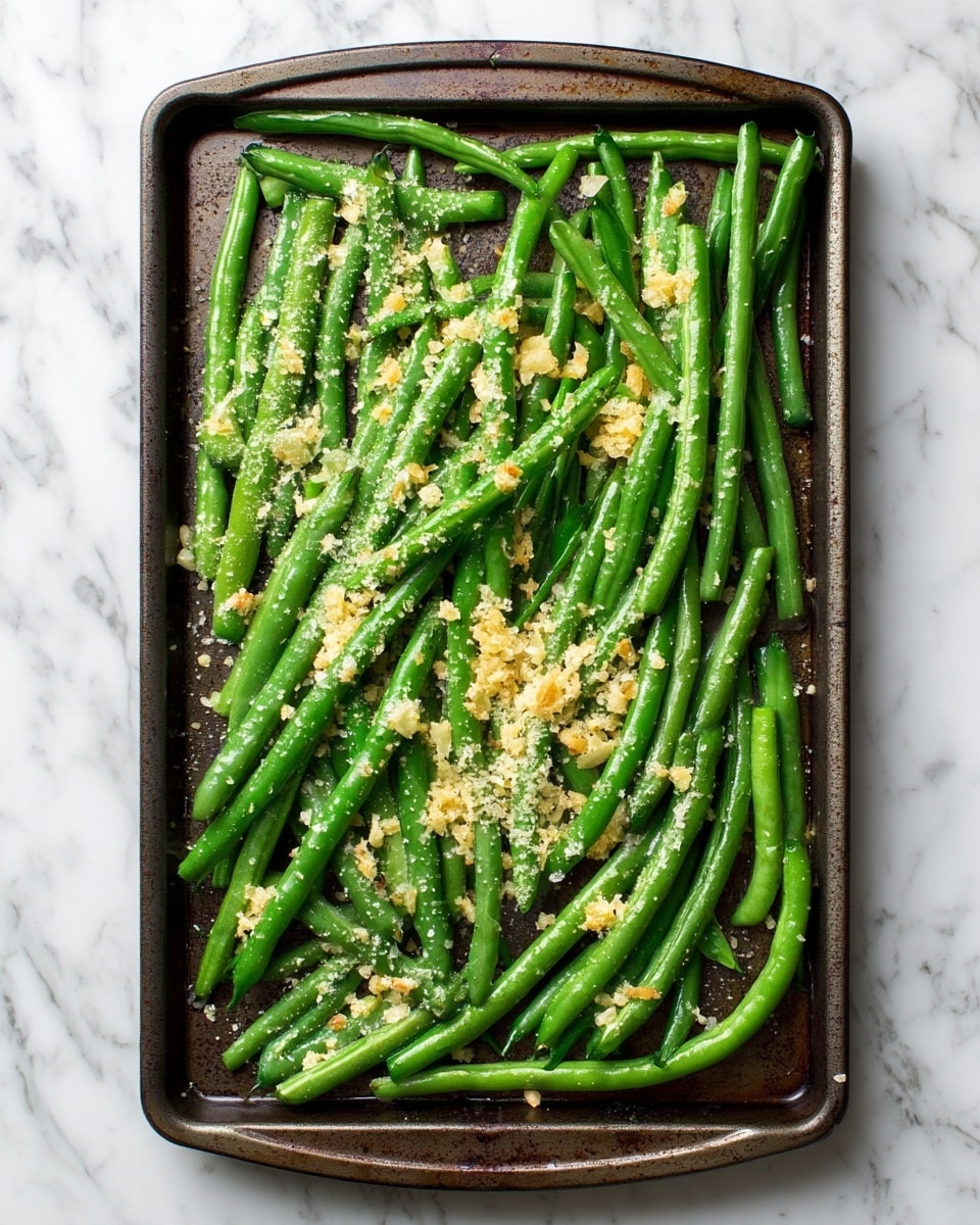 A dark metal baking tray filled with a single layer of fresh, bright green beans spread evenly across it. On top of the beans, small bits of light yellow garlic and white grated cheese are sprinkled unevenly, adding texture and contrast. The tray sits on a white marbled surface, creating a clean and bright background. Photo taken with an iphone --ar 4:5 --v 7