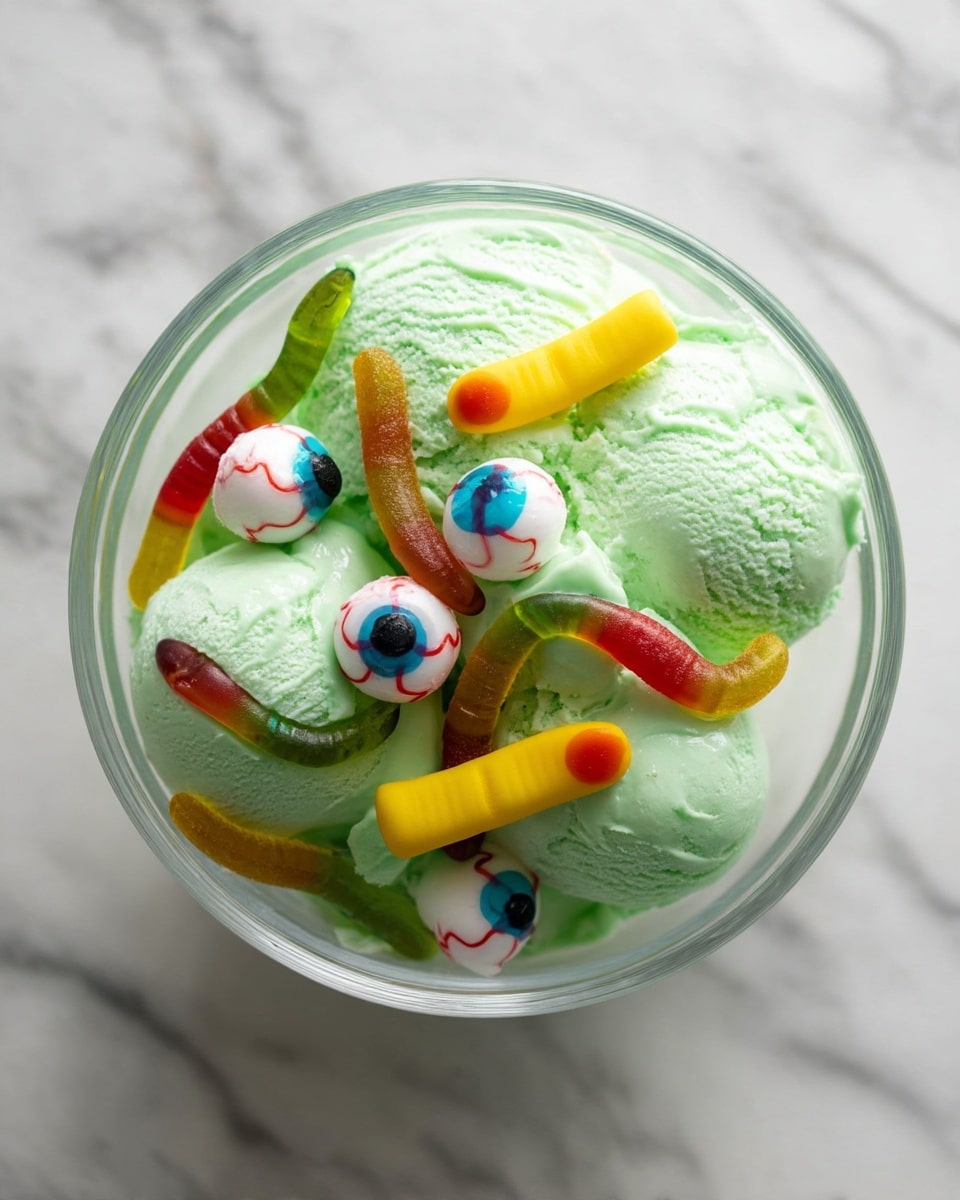 Zombie Punch for Kids Recipe 5 In this image, there is a clear glass bowl filled with light green ice cream with a fluffy, creamy texture. Floating on top are several round white candy eyeballs with blue irises and red veins, adding a spooky look. Scattered among the eyeballs are gummy worms in mixed colors of red, green, yellow, and brown, giving a slimy, playful appearance. At the front, there is a yellow gummy finger with a small red spot at the tip, resembling a nail. The bowl is placed on a white marbled surface. Photo taken with an iphone --ar 4:5 --v 7